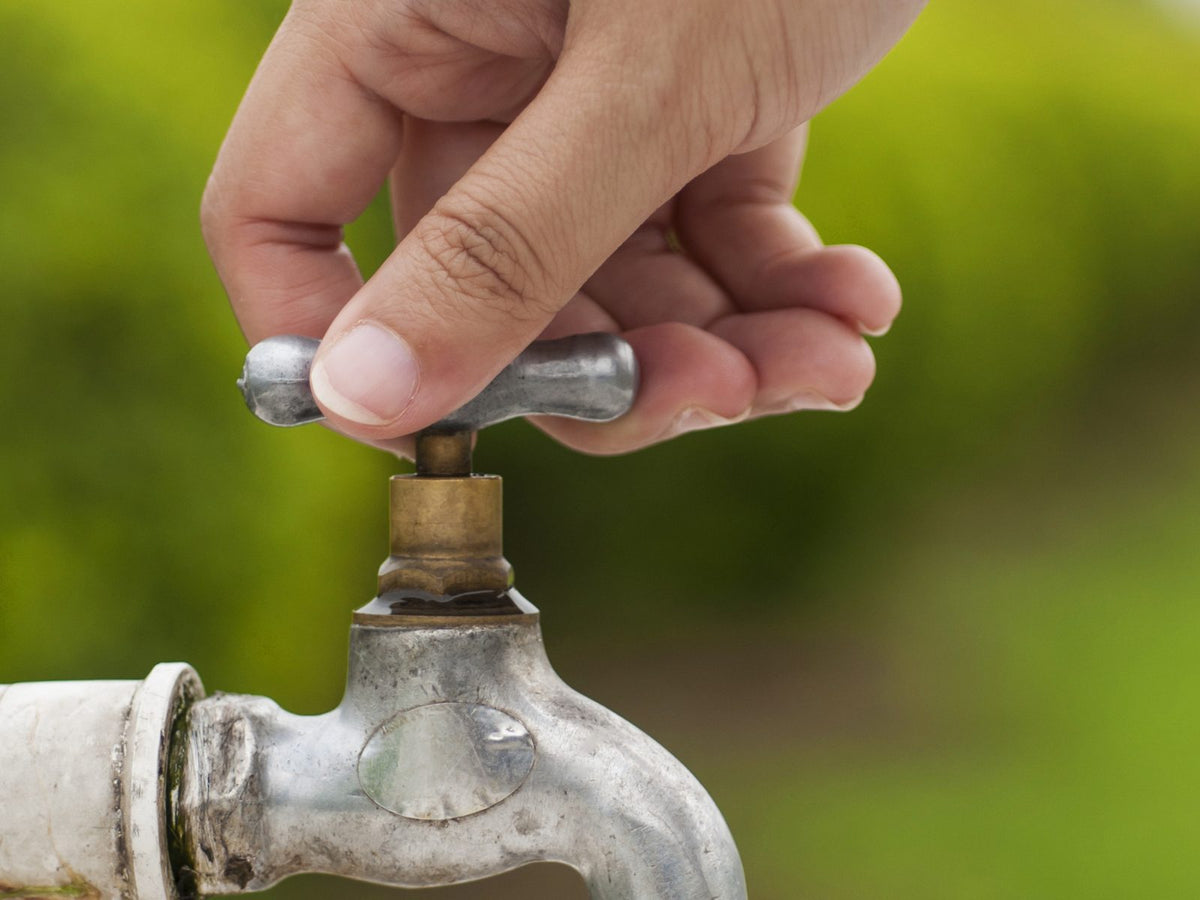 Main qui ferme un robinet extérieur de jardin, une goutte d'eau au bout du bec